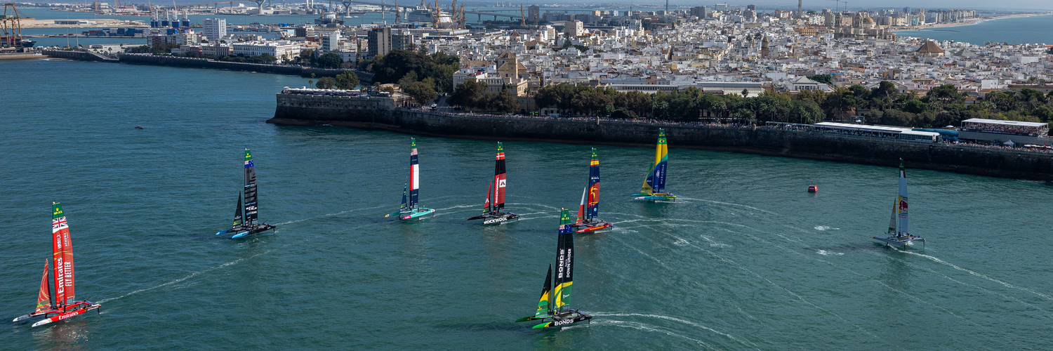 Emirates Great Britain SailGP Team helmed by Dylan Fletcher leads New Zealand SailGP Team helmed by Peter Burling, USA SailGP Team helmed by Taylor Canfield, ROCKWOOL Denmark SailGP Team helmed by Nicolai Sehested, Spain SailGP Team helmed by Diego Botin and Mubadala Brazil SailGP Team helmed by Martine Grael past the SailGP Race Stadium on Race Day 2 of the DP World Spain Sail Grand Prix held in Cadiz, Spain Sunday 5 October 2025
